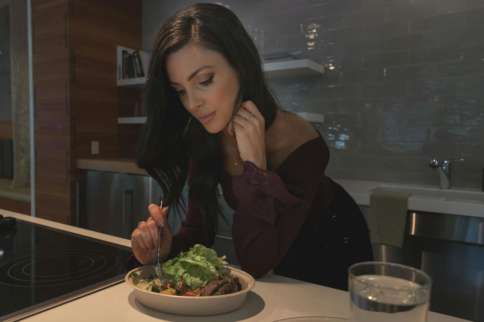 Kobieta o długich brązowych włosach je sałatkę w nowoczesnej kuchni