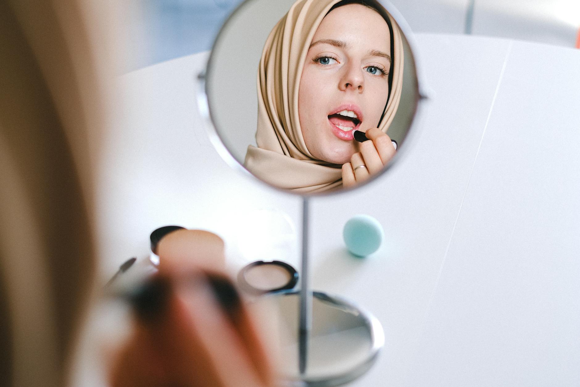 Kobieta w hijabie maluje usta, przeglądając się w lustrze