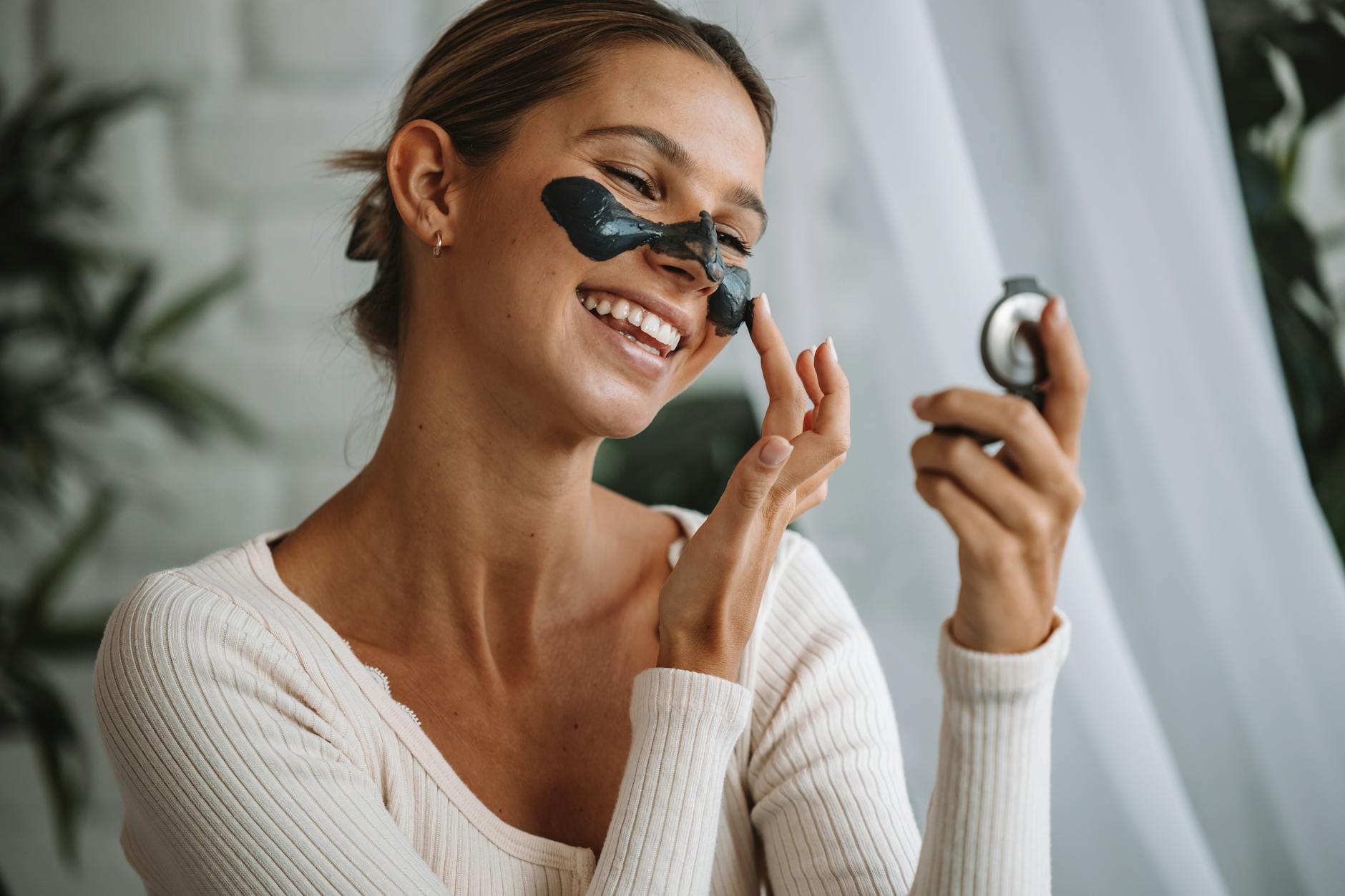 Uśmiechnięta kobieta nakłada maseczkę na twarz, patrząc w lustro