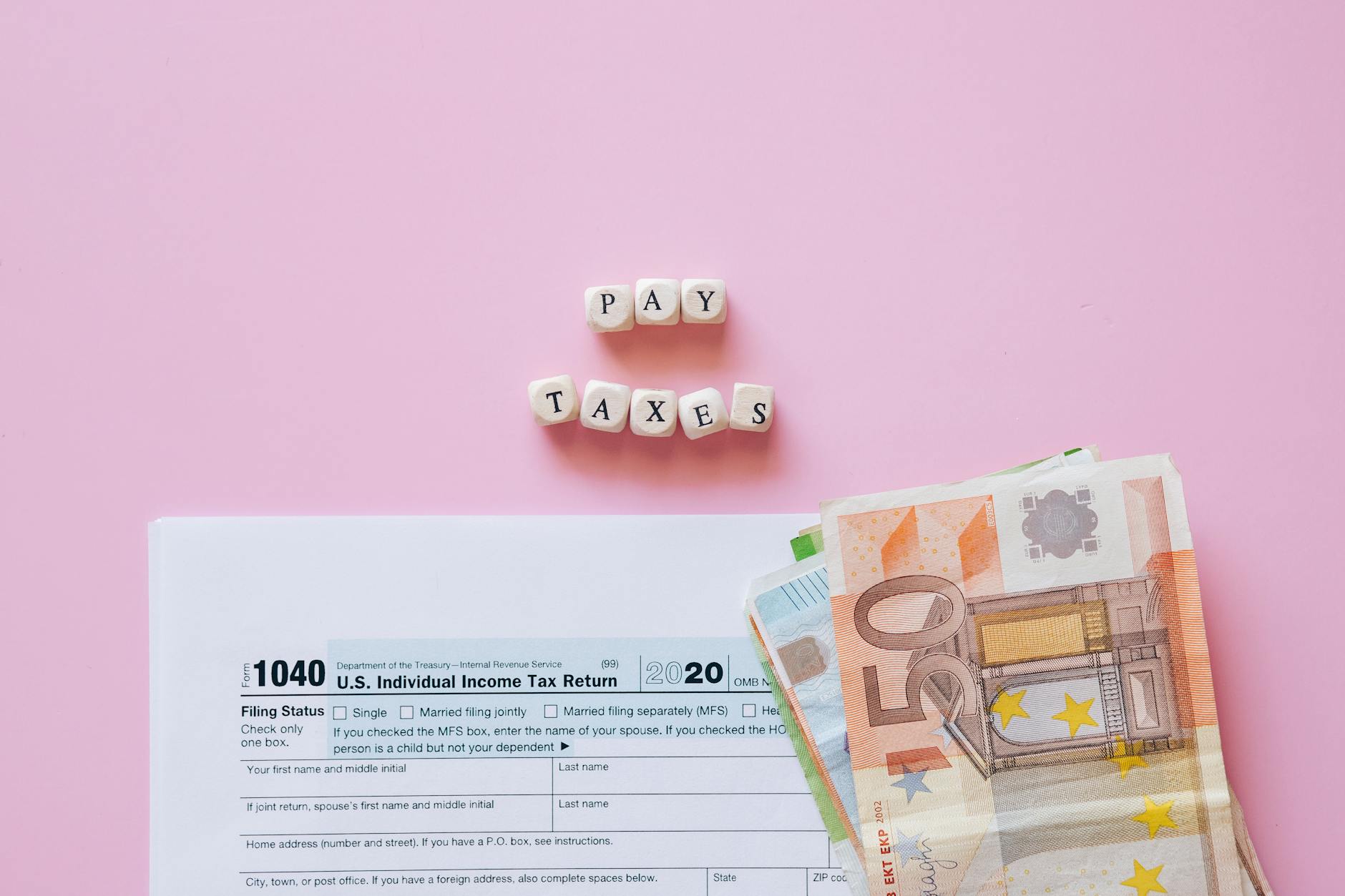 Formularz podatkowy, banknoty euro i klocki z napisem Pay Taxes na różowym tle