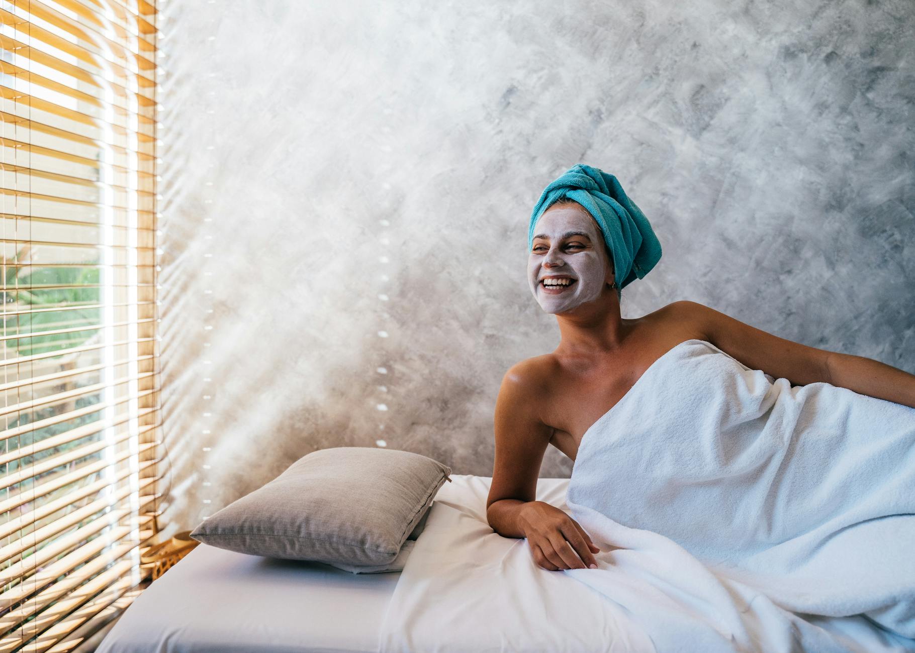 Kobieta z maseczką na twarzy relaksuje się w spa, owinięta ręcznikiem