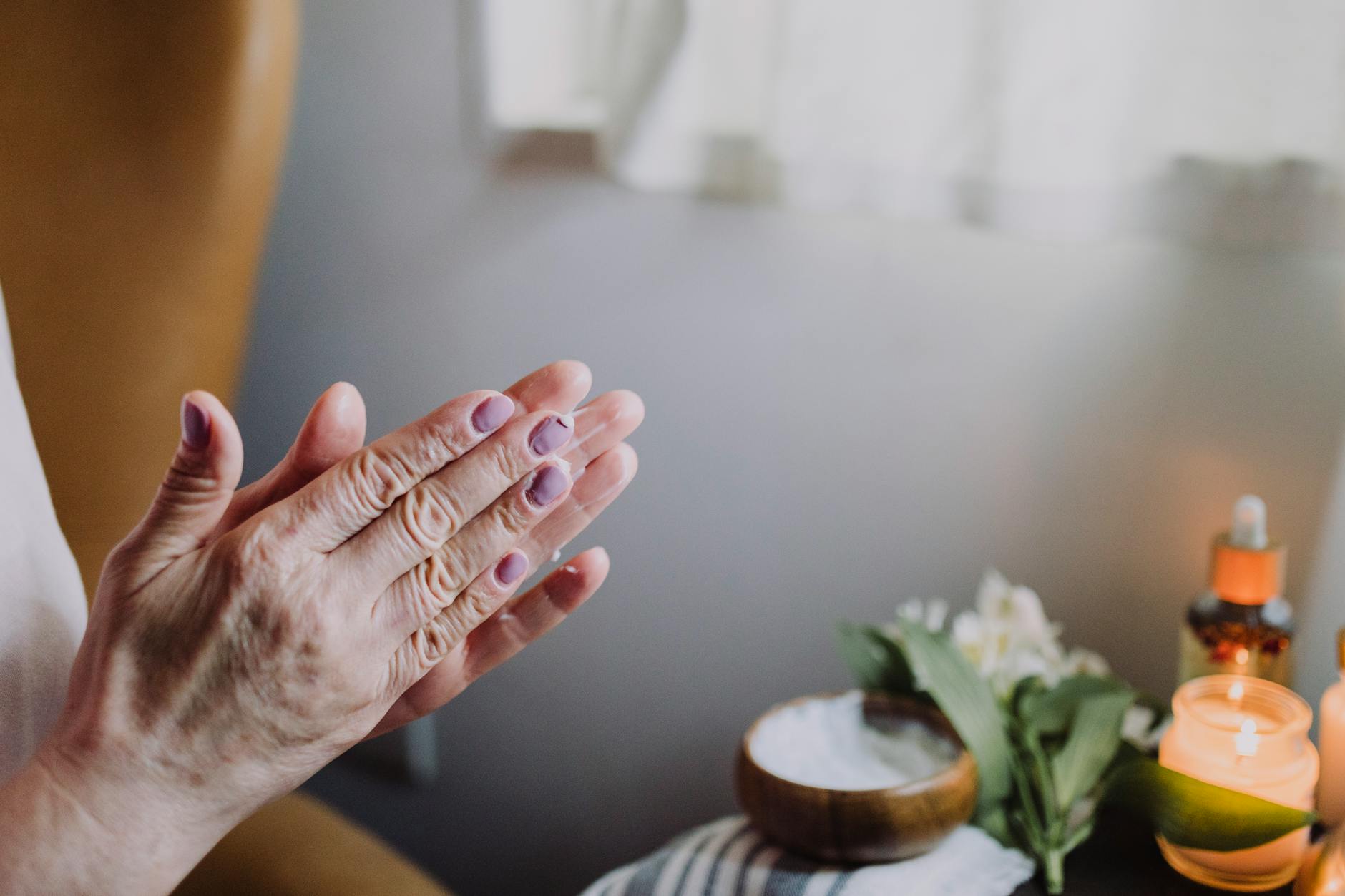 Dłonie nakładające kosmetyk pielęgnacyjny przy świecach w relaksującej scenerii