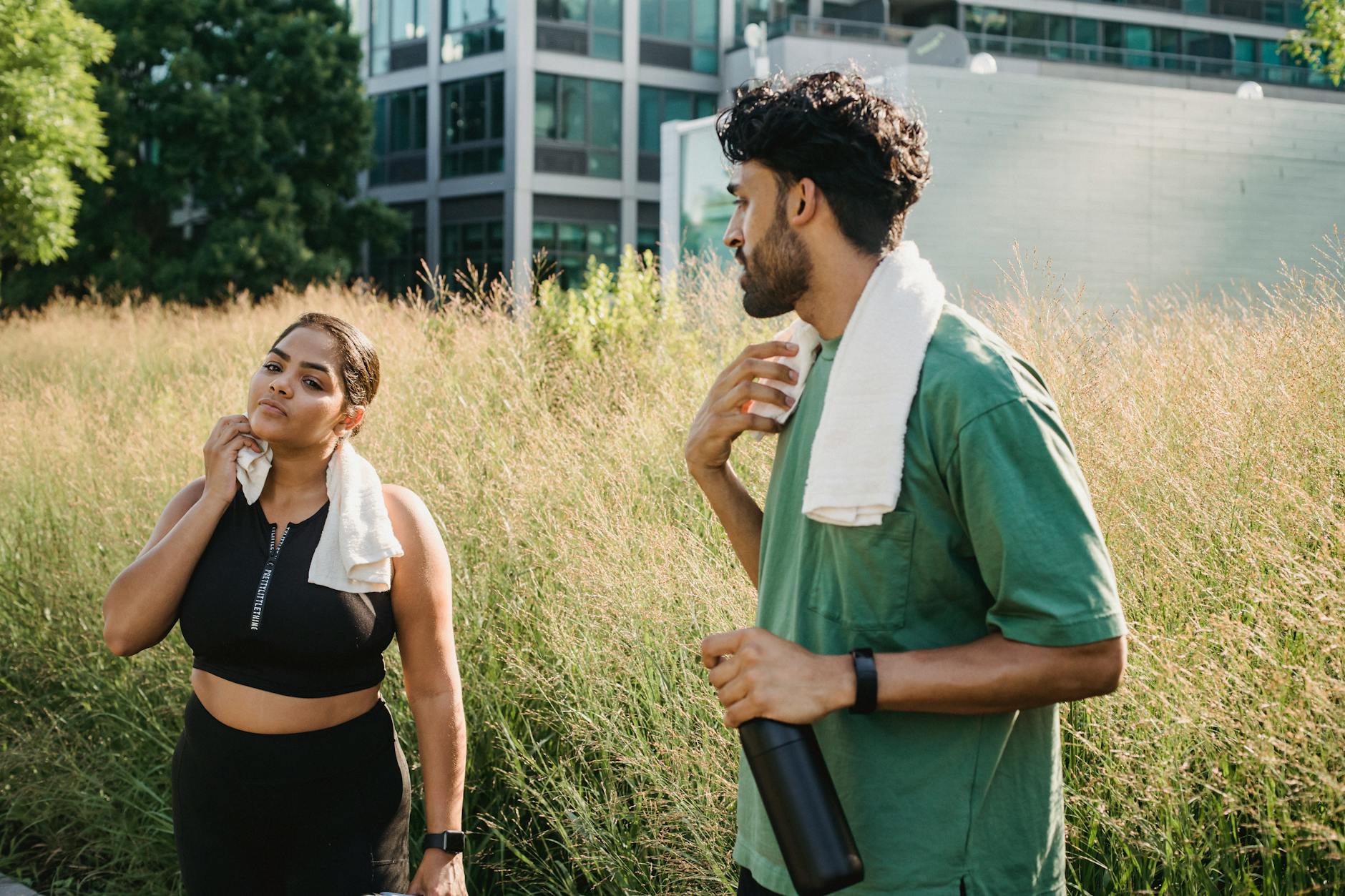 Dwie dorosłe osoby rozciągają się po treningu w letnim parku miejskim
