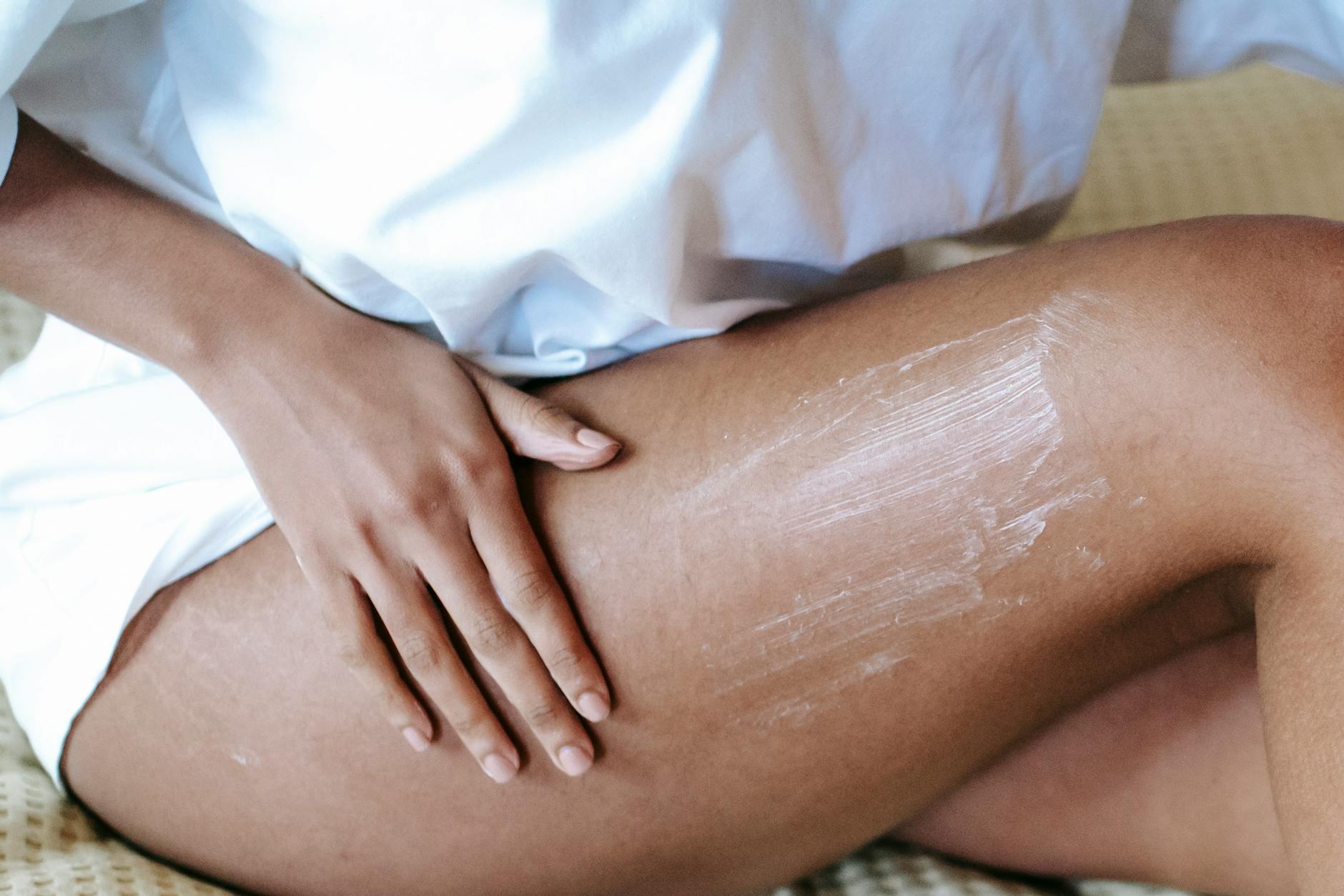 Kobieta siedząca na łóżku nakłada krem na skórę biodra po depilacji