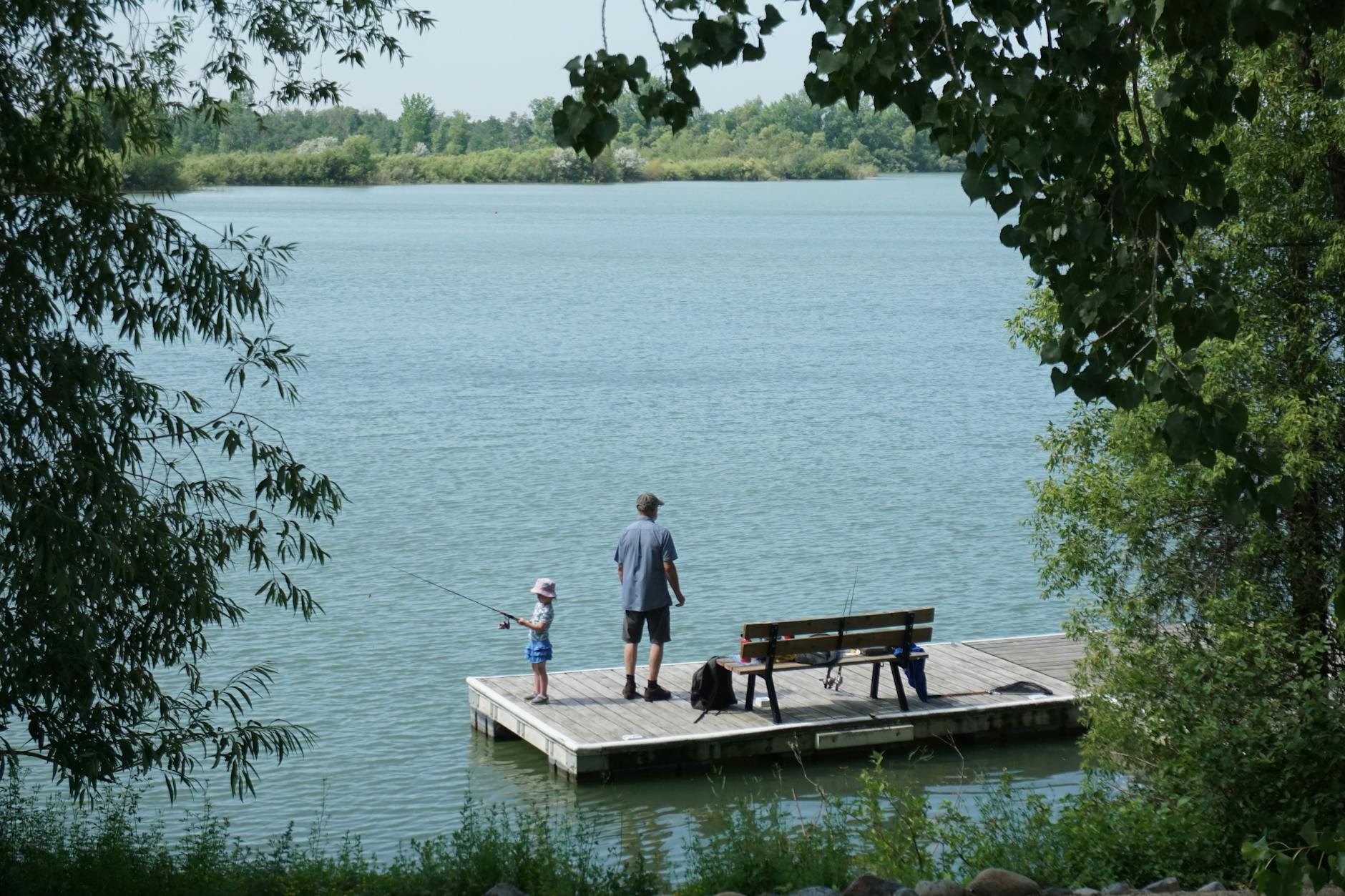 Ojciec uczy córkę wędkować na pomoście nad spokojnym jeziorem