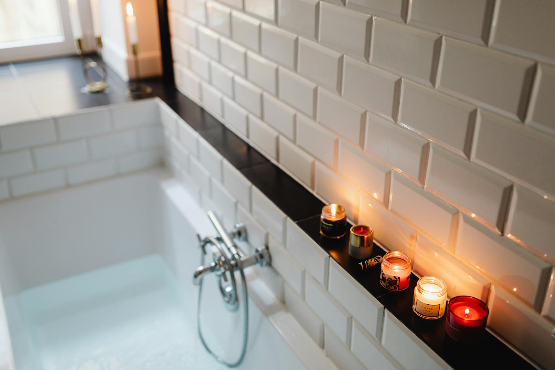 Rytuał „quiet luxury” w domu: minimalizm, jakość kosmetyków i wolniejsze tempo Przytulna łazienka z zapalonymi świecami i napuszczoną wanną do relaksu