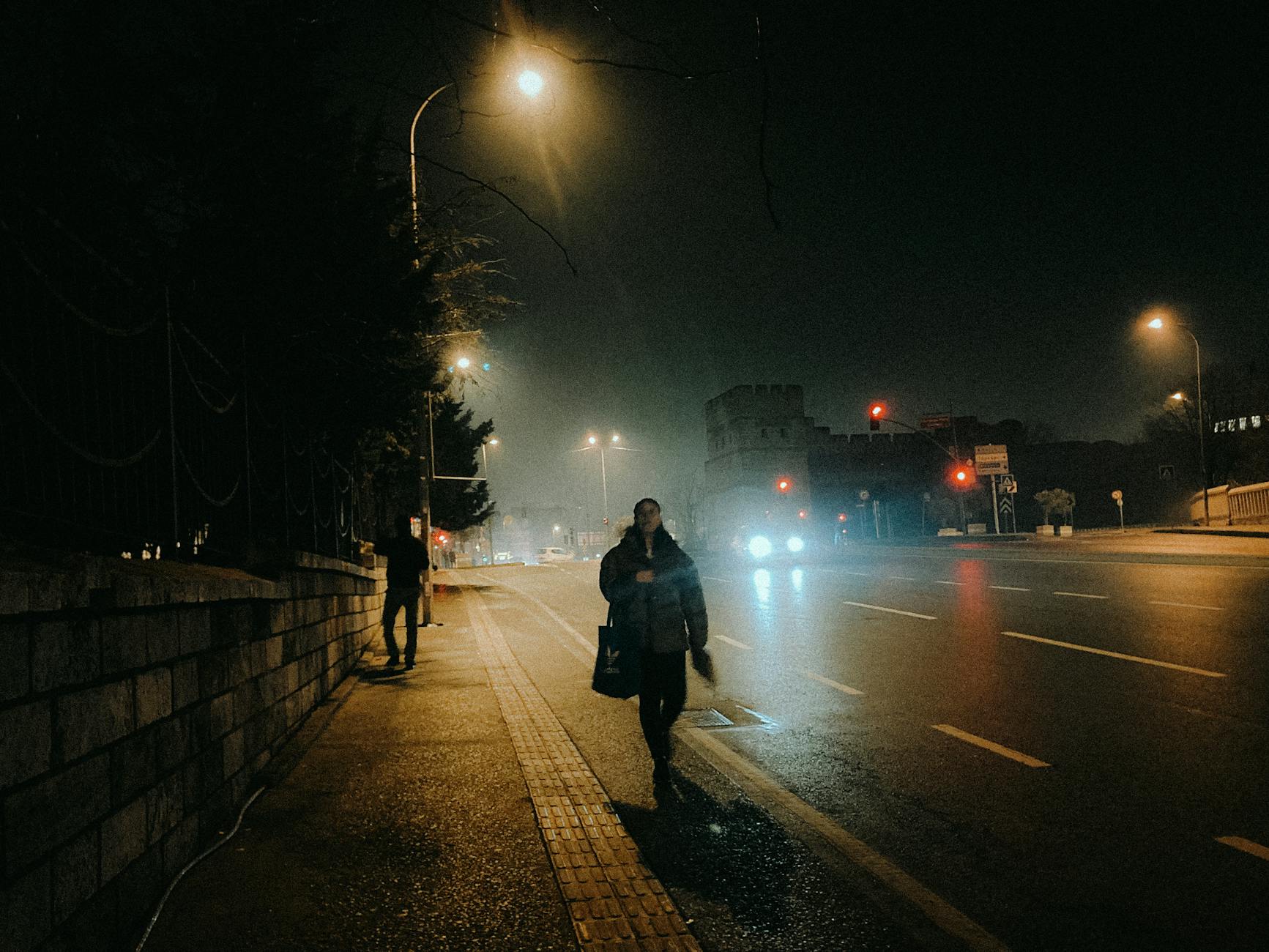 Nocna ulica w mieście z przechodniami na słabo oświetlonym chodniku Nocna ulica w mieście z przechodniami na słabo oświetlonym chodniku